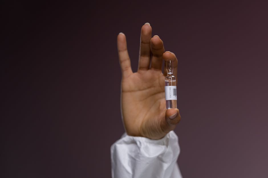 A detailed photo of a hand in gloves holding a vaccine ampoule against a neutral background.