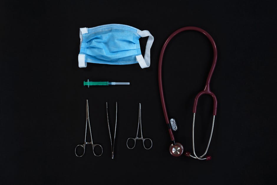 Top view of medical tools including a mask, syringe, and stethoscope on a black surface.